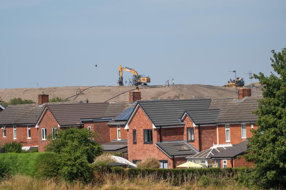 Homes with a large landfill and excavators looming behind them.