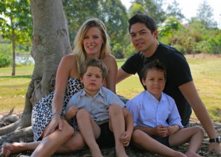 A couple with two young boys sitting on the ground next to a tree.