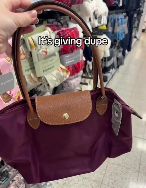 A hand holding a purple handbag with brown leather accents and a tag that reads "Originals" in a store aisle.
