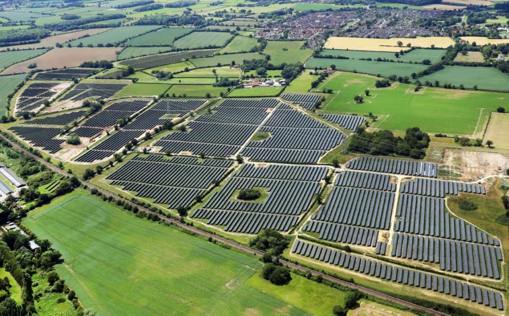 Aerial view of a large solar farm in the countryside, next to agricultural fields and a town.