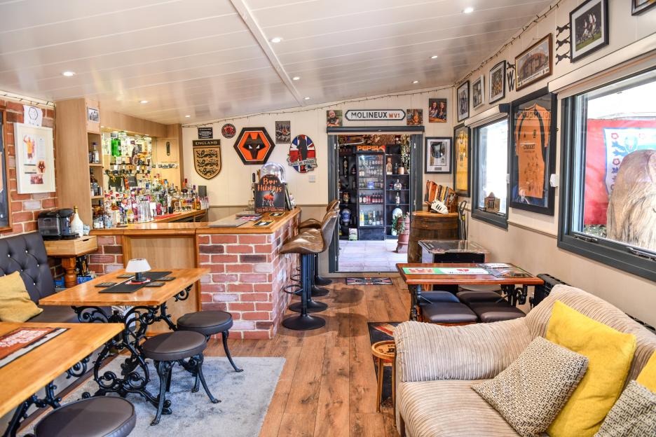 Interior of Bar Hibby's, a DIY back garden pub shed with a full bar, pub benches, a TV, and Wolverhampton Wanderers FC memorabilia.