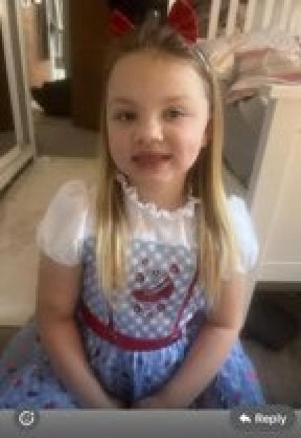 A young girl with long blonde hair and red bows in her hair, wearing a white and blue dress.