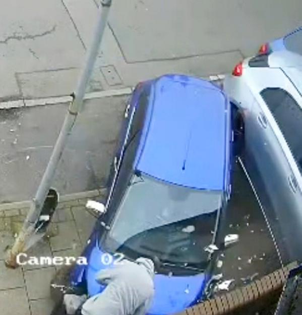 An overhead view of a blue car crashed into a wall, with a person crouching next to it.