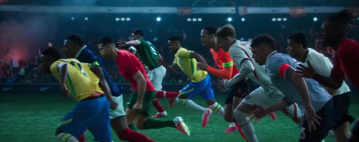A group of international soccer players in uniforms of different colors runs across a green field.