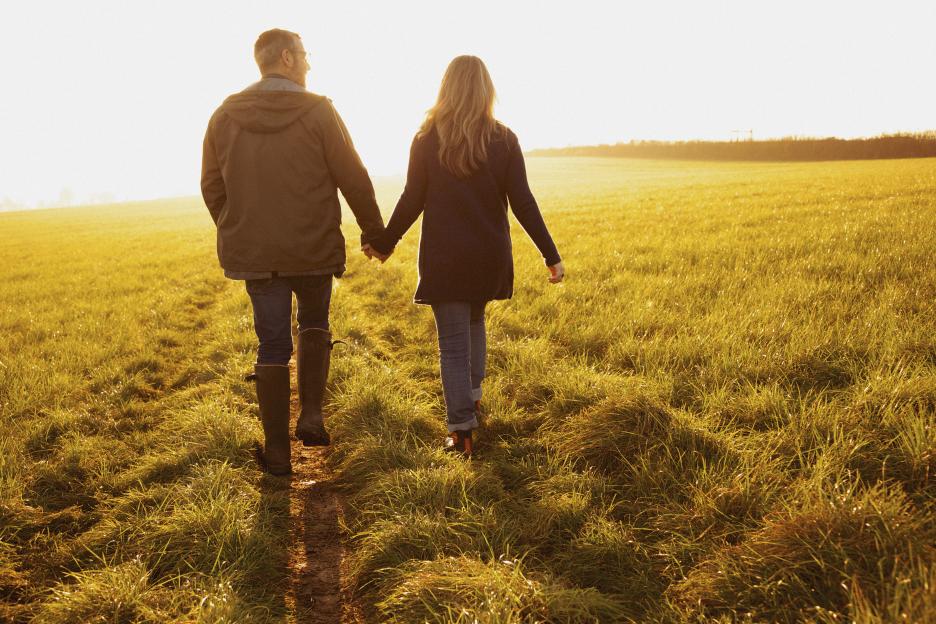 Couple walking hand in hand through a sunlit field.
