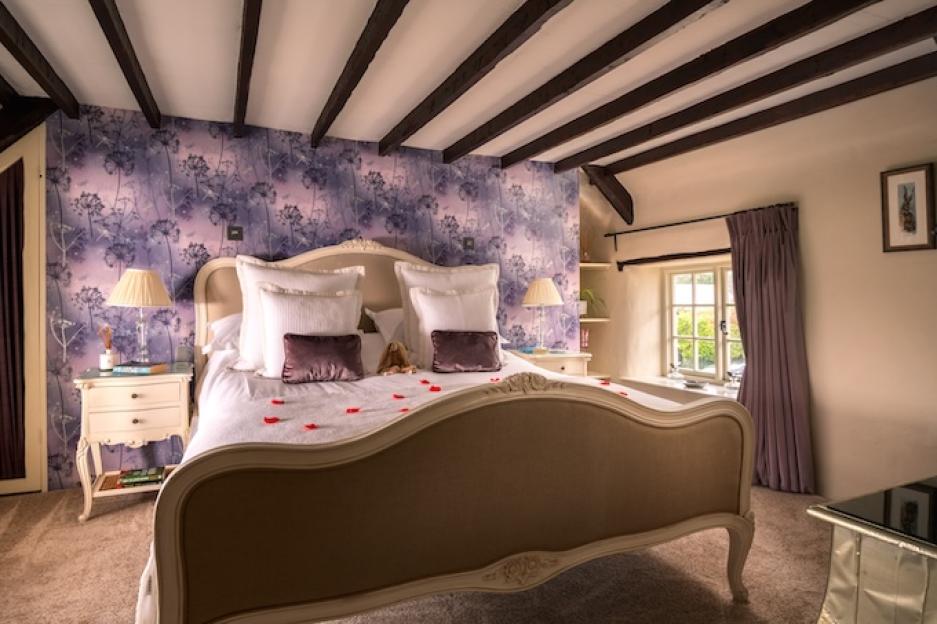 Bedroom at Rose Cottage Devon with a bed, purple floral wallpaper, and exposed wooden beams.