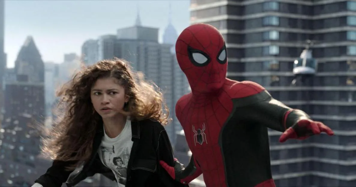 Spider-Man in a red and black suit holds onto MJ, who has wild hair, against a backdrop of city buildings.