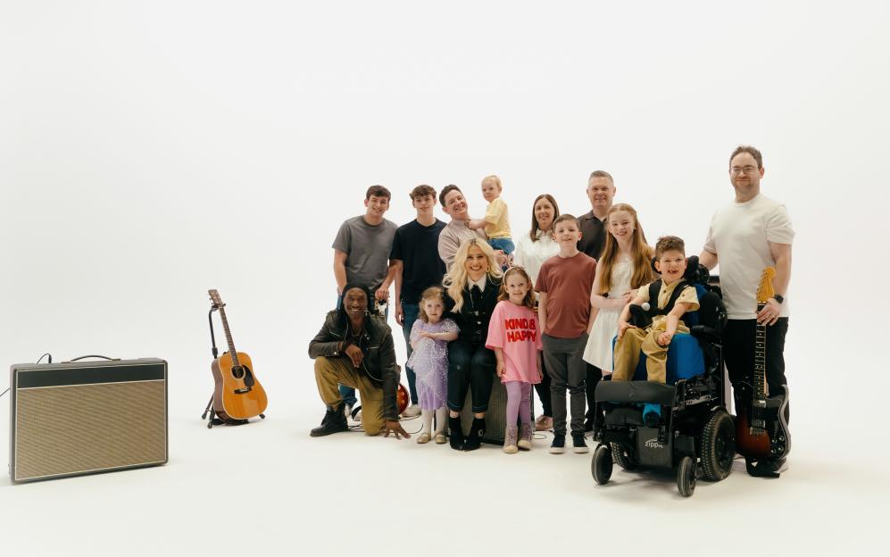 A group of adults and children with musical instruments, including a child in a wheelchair, posing for a photo.