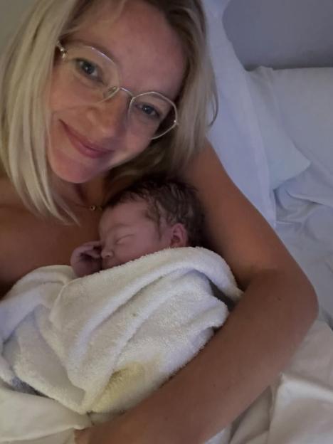 A woman in glasses holds a swaddled sleeping baby.