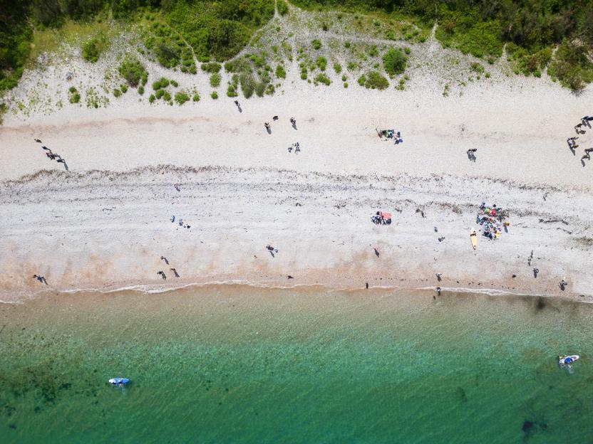 Aerial view of Elberry Cove beach in South Devon, with people on the sandy shore and in the clear green water.