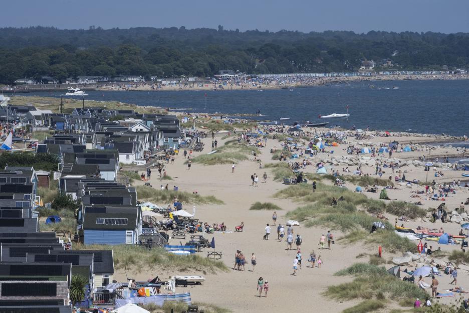 Aerial view of Mudeford beach in Dorset with numerous people, beach huts, and boats.