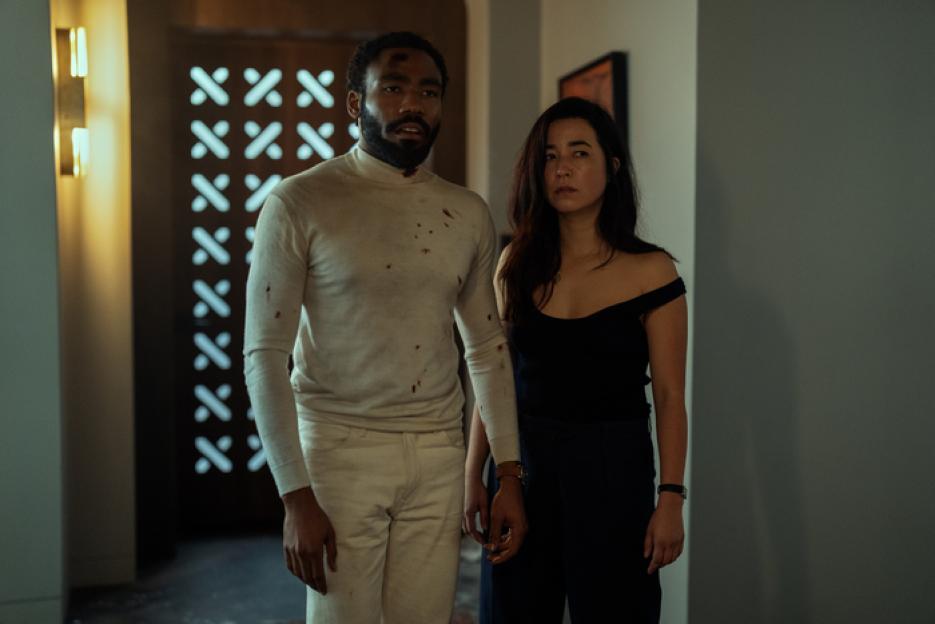 Donald Glover, with blood on his shirt, and Maya Erskine looking serious.