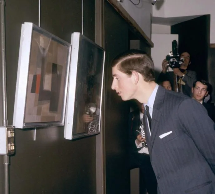 Prince Charles looking closely at two abstract paintings hanging on a wall in a gallery.
