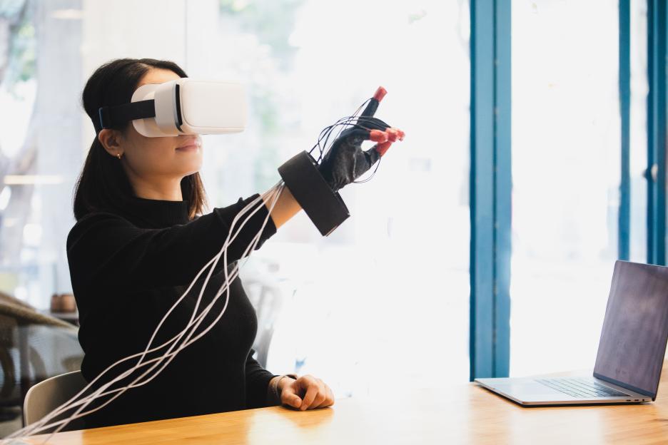 asian woman wearing VR headset and haptic glove interacting with virtual object/person in the metaverse