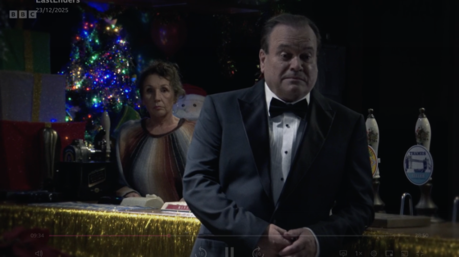 A Christmas scene from EastEnders with a man in a tuxedo and a woman behind a bar.