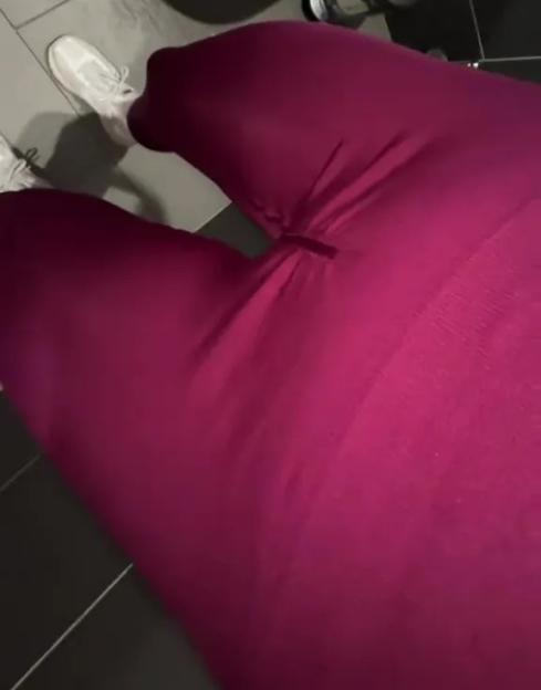 A woman standing in magenta leggings with a hole near the crotch, in front of a toilet.