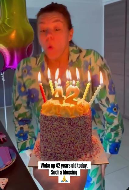 Woman blowing out candles on a birthday cake that spell "42."