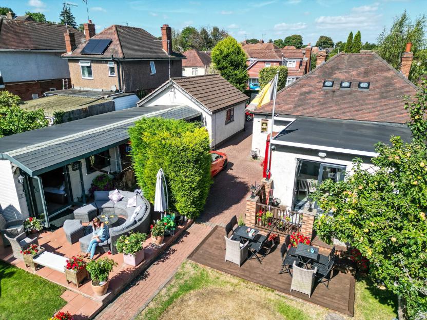 Aerial view of a backyard with a woman sitting on a patio lounge next to a bar shed and outdoor dining tables.