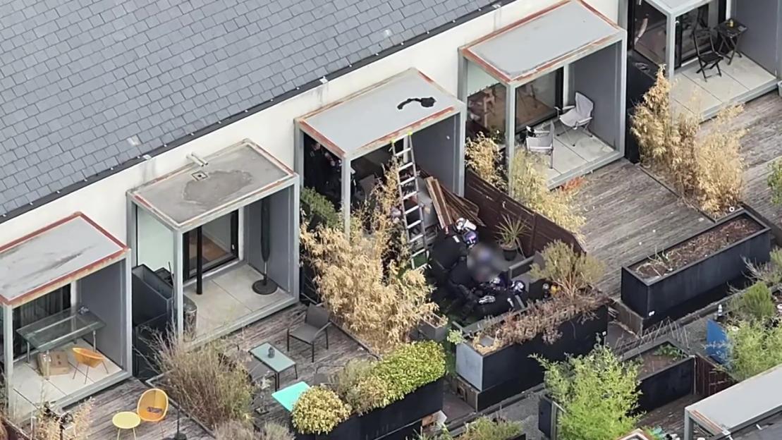 Police officers arresting a man on a rooftop balcony.