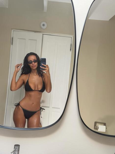 Maya Jama taking a selfie in a black studded bikini and sunglasses.