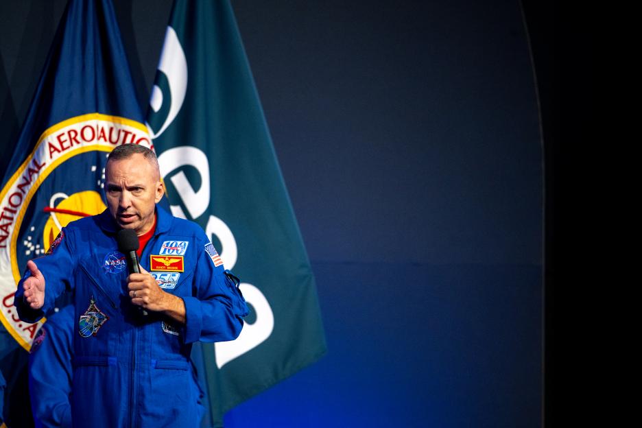 Astronaut Randy Bresnik, in a blue flight suit, speaks into a microphone at the Artemis III crew announcement.
