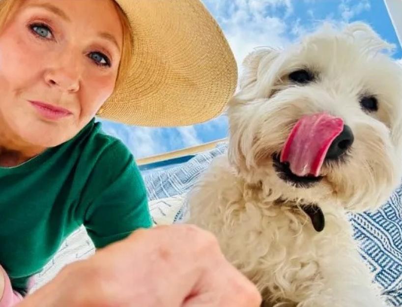 J.K. Rowling taking a selfie with a white dog licking its snout.