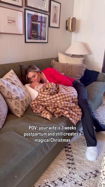 Sophie Habboo in a red top, kissing her newborn baby, who is wrapped in a brown plaid blanket, on a green couch.