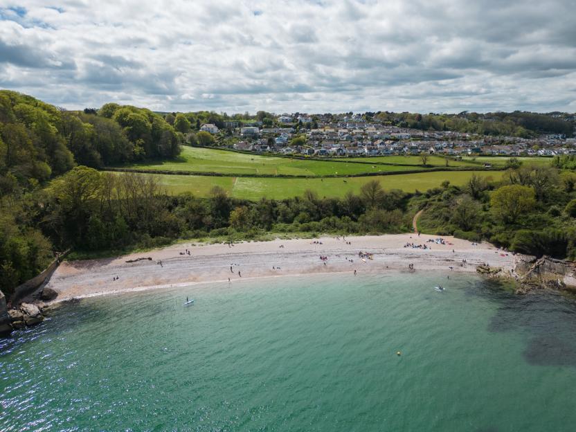 Aerial view of Elberry Cove Beach in Torbay, South Devon, with people on the sandy beach and clear blue sea.