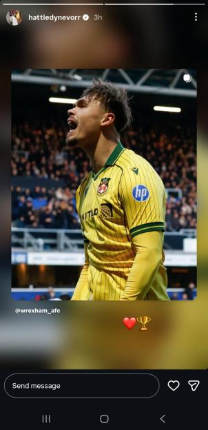A male Wrexham footballer in a yellow and green jersey, shouting on the field with a crowd in the background.