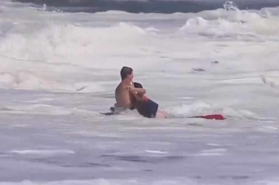 A 16-year-old in red shorts rescues a 10-year-old boy from rough waves.