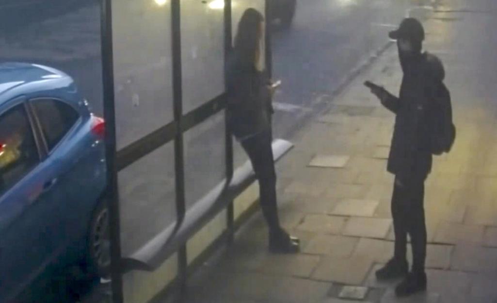a man is looking at his phone next to a woman at a bus stop