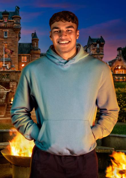 Faraaz, an Internal Auditor from Middlesbrough, smiling in front of a castle and fire pit.