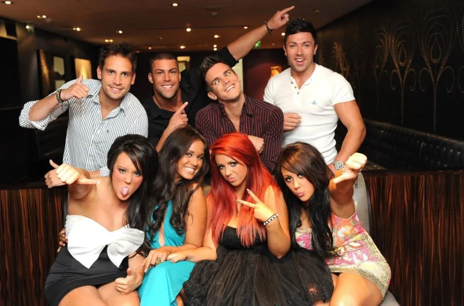 The Geordie Shore cast posing together, featuring Gaz Beadle, Jay Gardner, James Tindle, Charlotte Leticia Crosby, Vicky Pattison, Holly Hagan, and Sophie Kasaei.