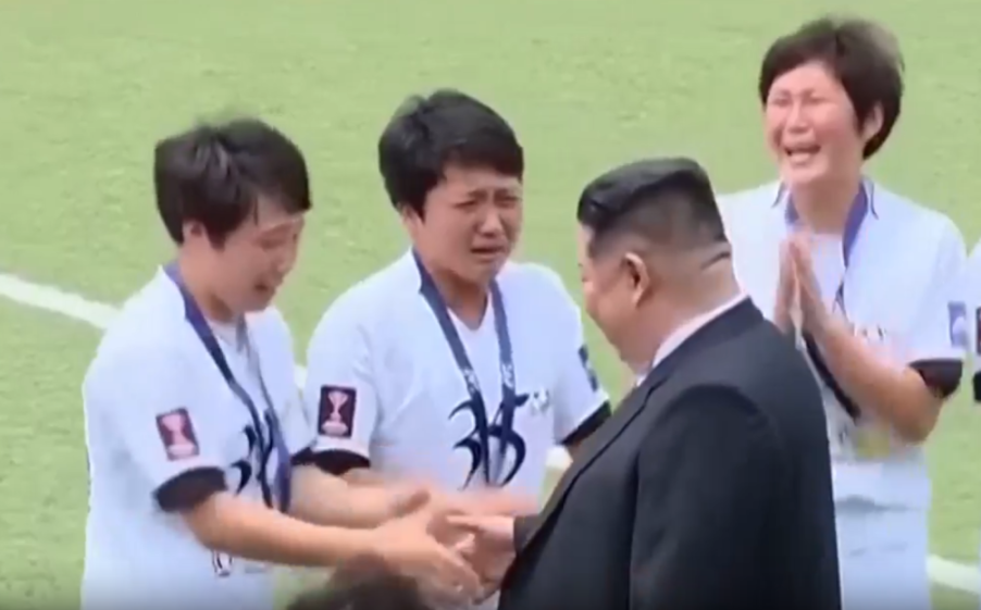 North Korean leader Kim Jong Un shaking hands with a crying woman in a white uniform while other women in uniform cry around them.