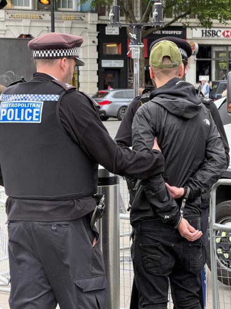 A Metropolitan Police officer detaining a person in handcuffs at Kings Cross Station during a protest.