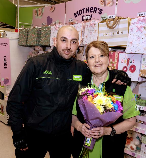 Charlie and his mother Maggie, both Asda employees, pose in an Asda store display for Mother's Day, Maggie holding a bouquet of flowers.