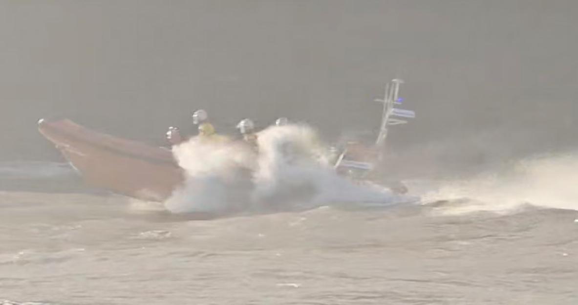 A rescue boat navigating through rough waters, with spray rising from a large wave.