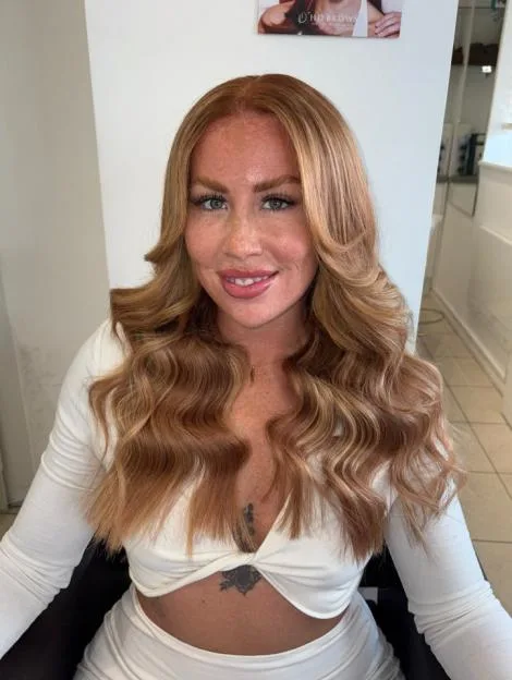A woman with long wavy blonde hair and a white dress smiles at the camera.
