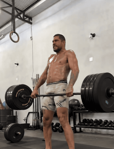 A muscular, shirtless man doing a deadlift in a gym.