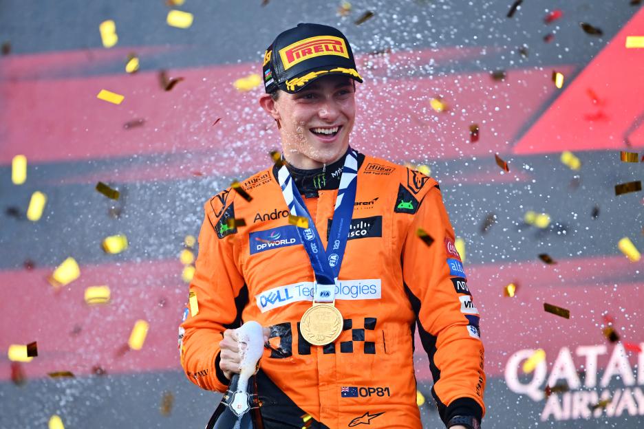 Oscar Piastri celebrates his win at the F1 Grand Prix of Azerbaijan, holding a bottle of champagne and wearing a medal as confetti falls around him.