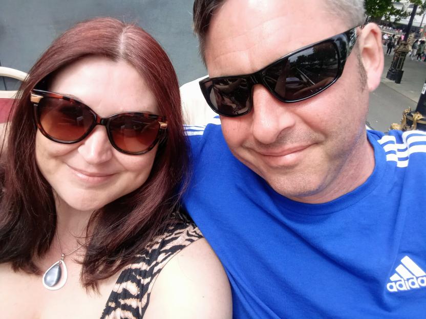 A couple wearing sunglasses smiles for a close-up selfie.