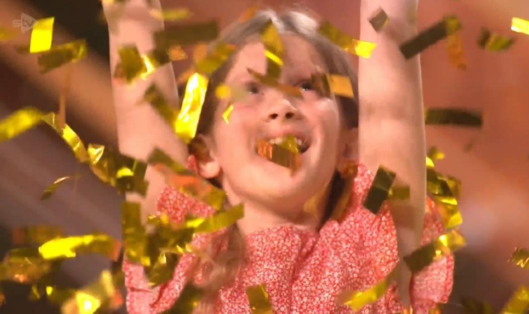 A young girl with her arms raised in celebration as golden confetti falls around her.