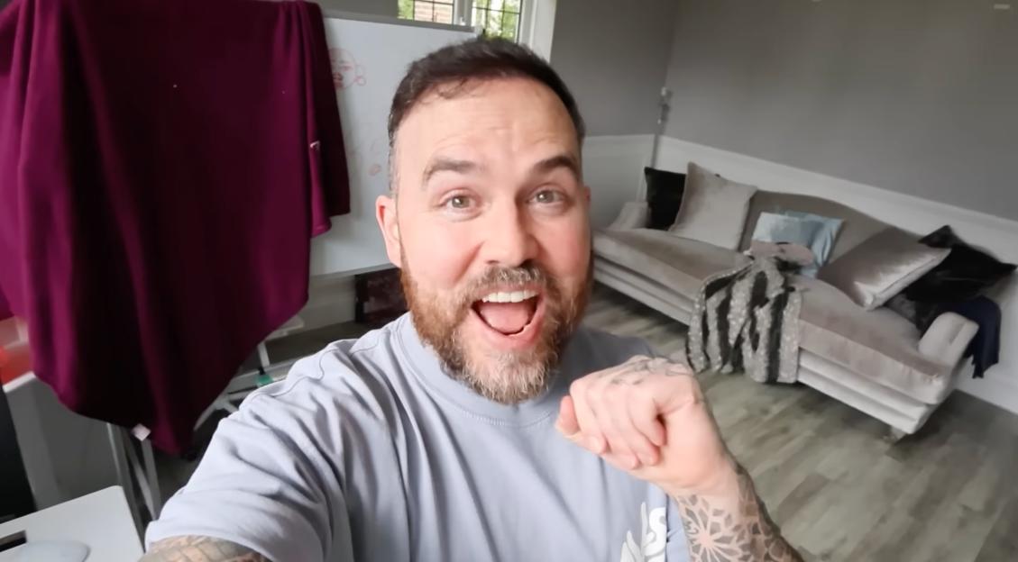 Jonathan Joly with a fist and open mouth, wearing a light blue t-shirt and showing tattoos on both arms.