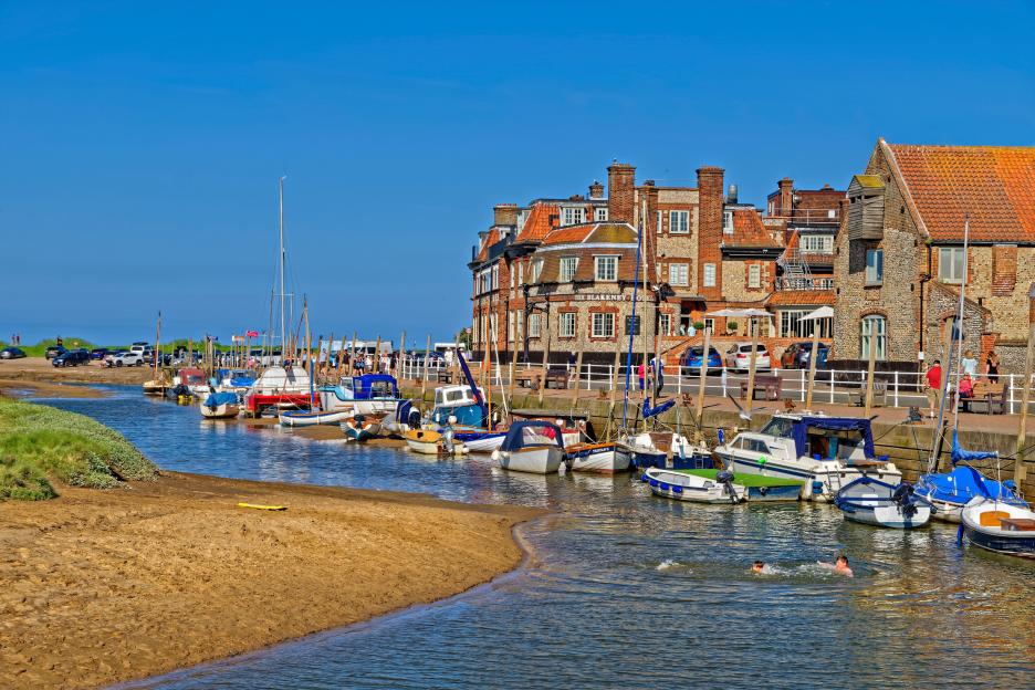 The Quay at Blakeney in Norfolk, England, with boats in the water and buildings along the shore.