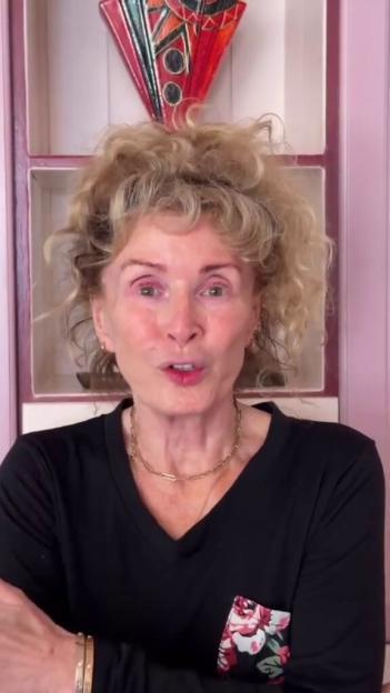 Beverley Callard wearing a black top with a floral print pocket and a gold necklace.