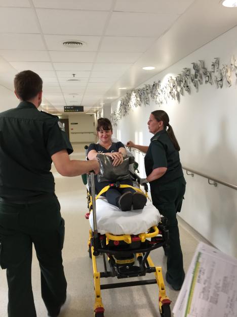 Esther Stanhope on a gurney being transported by two medical workers.