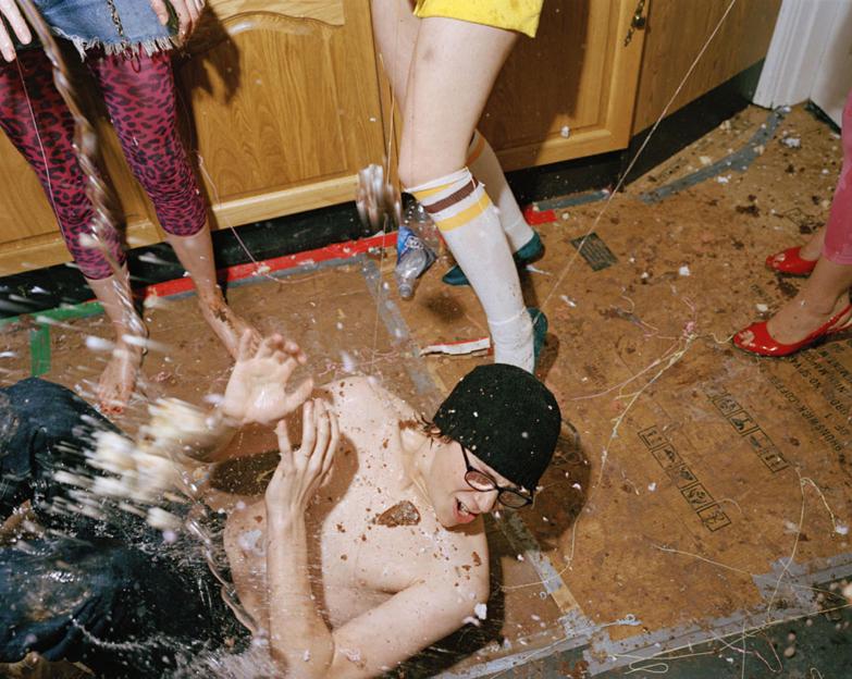 Still from Skins featuring Mike Bailey as Sid covered in a messy substance, with the legs of several other people surrounding him.