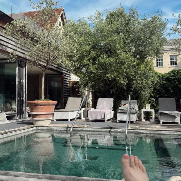 A foot in the foreground of a swimming pool with lounge chairs and trees in the background.