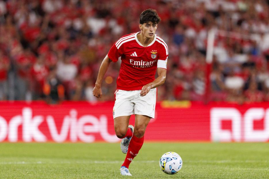 A soccer player in a red jersey and white shorts dribbles the ball on a green field.