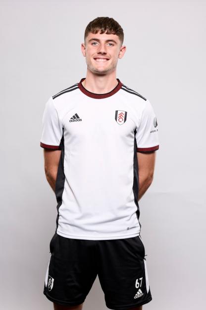 A young male footballer in a white Fulham U23 jersey, black shorts with number 67, and black and red trim, smiling at the camera.